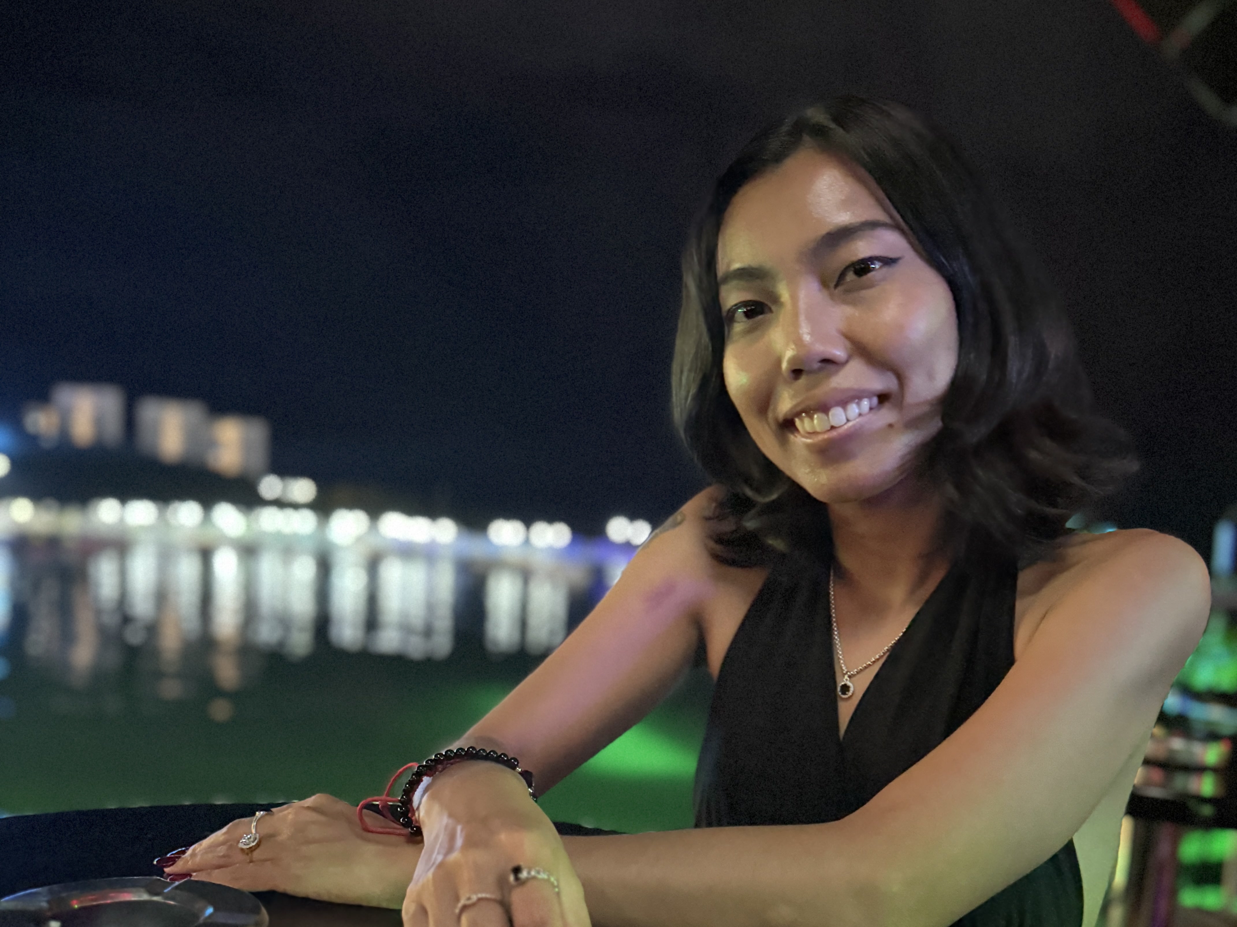 Siriwan smiles at an outdoor table beside the water at night.