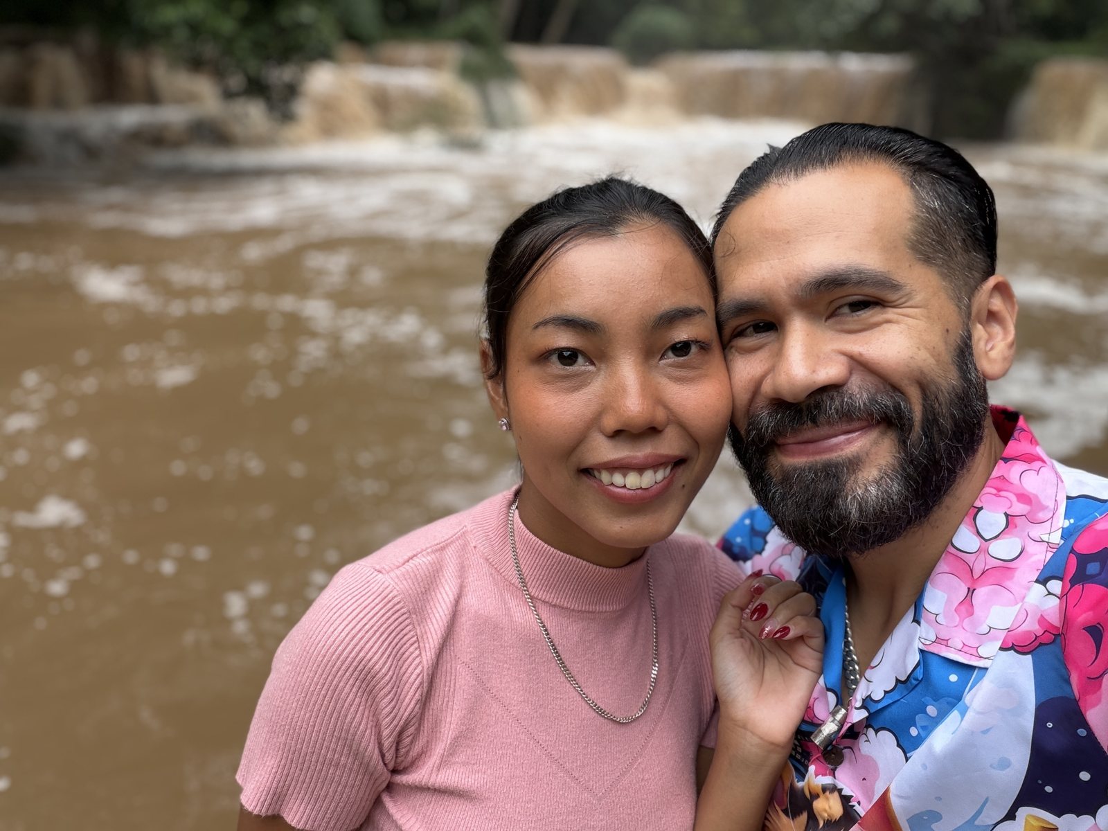 Josh and Siriwan beside a waterfall carrying brown water after heavy rain.